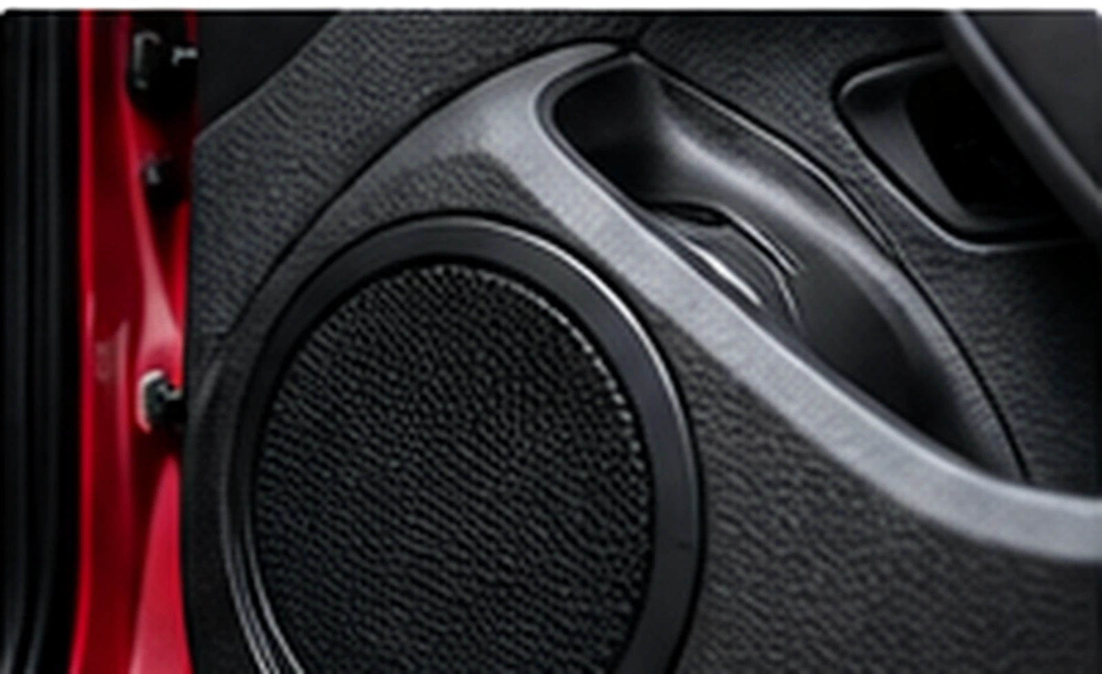 Close-up of a black speaker grille integrated into a red car door